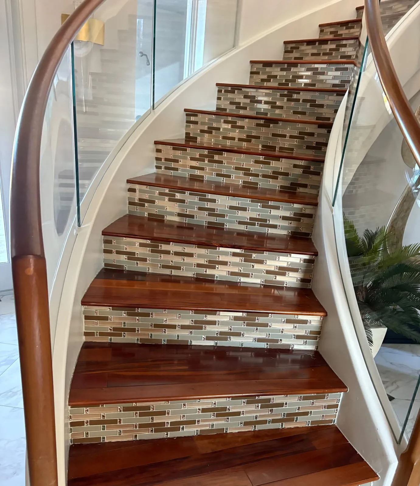 Curved staircase with wood treads, glass tile risers, and glass railings