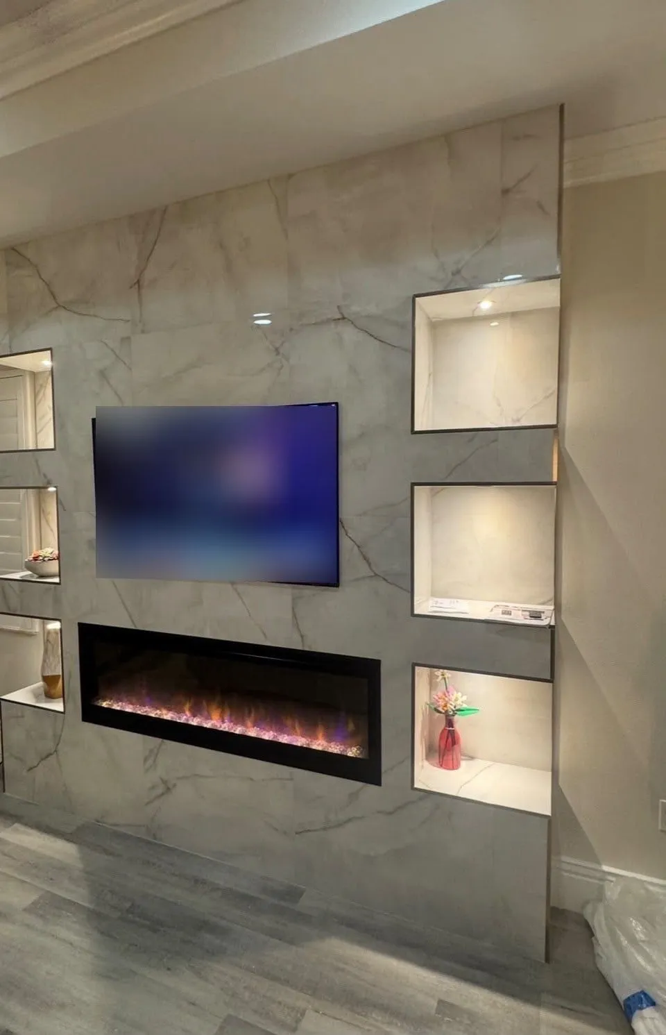 Finished feature wall with marble-look tile, an electric fireplace, and lit shelves